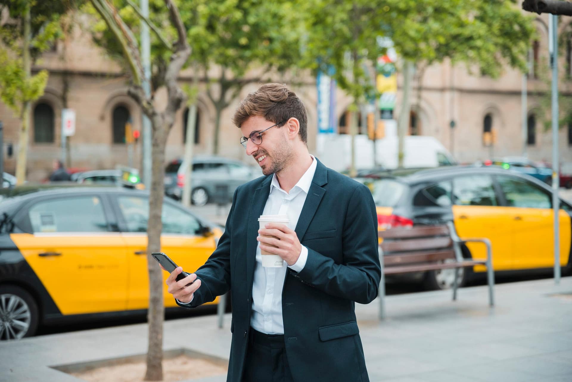 young businessman holding coffee cup looking mobile phone scaled